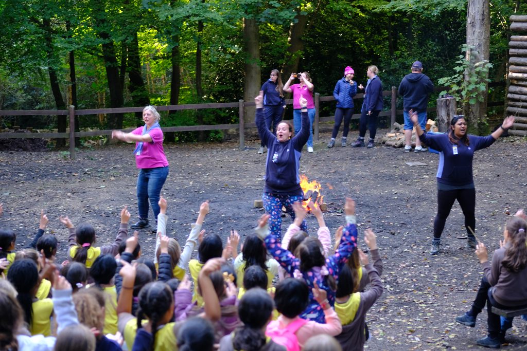 Three leaders, one in pink and two in blue, perform the actions to a song as the Brownies join in.