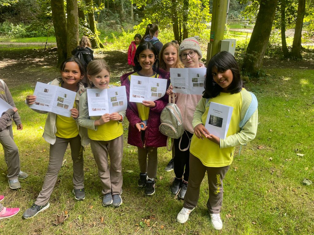 Six Brownies in their uniforms standing in front of trees. They hold up their Woodland Trail booklets.