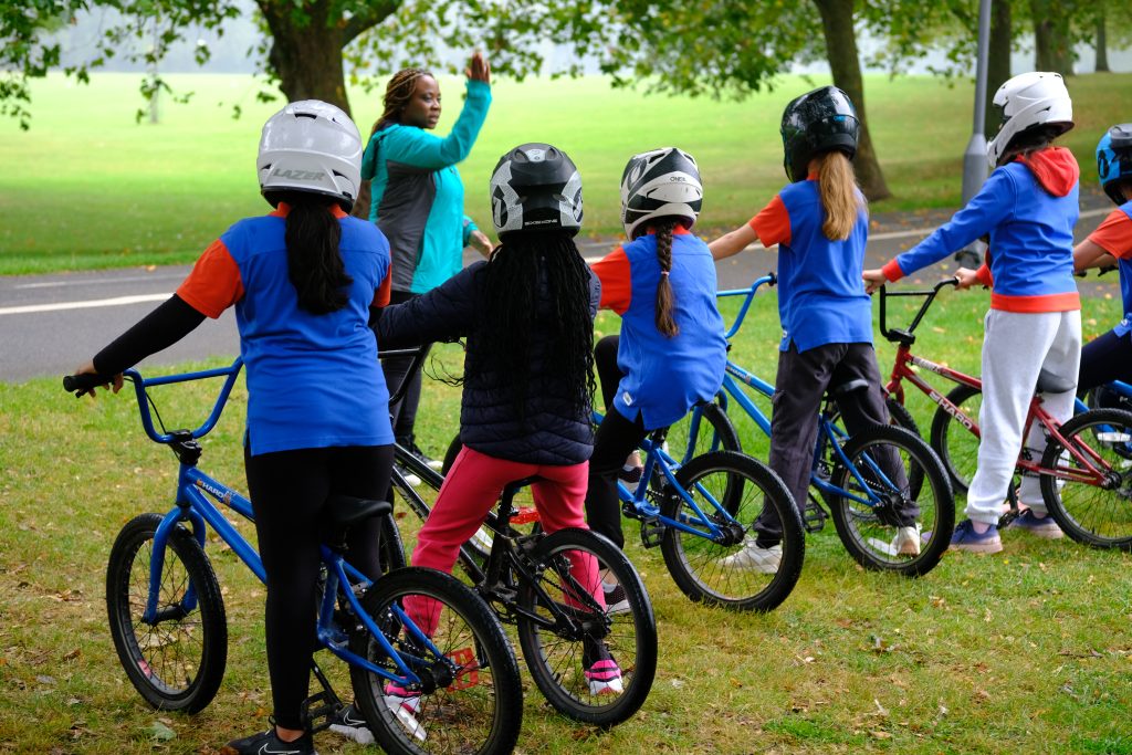 Four Guides in cycling helmets stand with their bikes watching an instructor.
