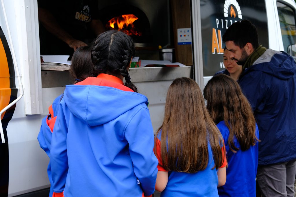 Guides standing in front of the pizza truck hatch, waiting for their pizzas.