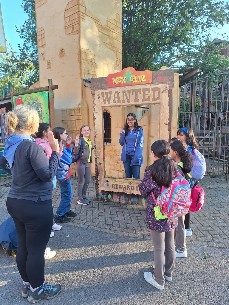 A Young Leader taking her promise inside a Wanted frame. The Brownies, Guide and Adult Leader stand around.