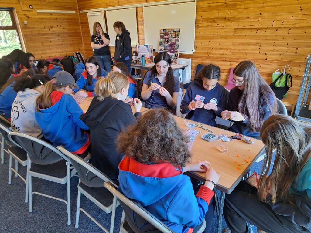 Guides and Rangers sitting around a long table making their beaded bracelets.